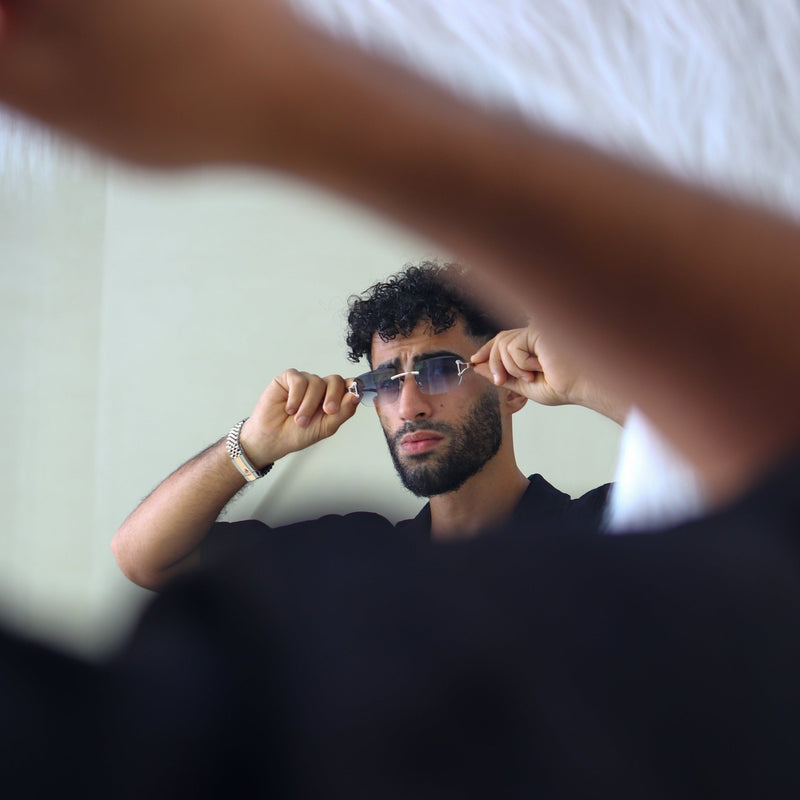 Man adjusting sunglasses in front of a mirror